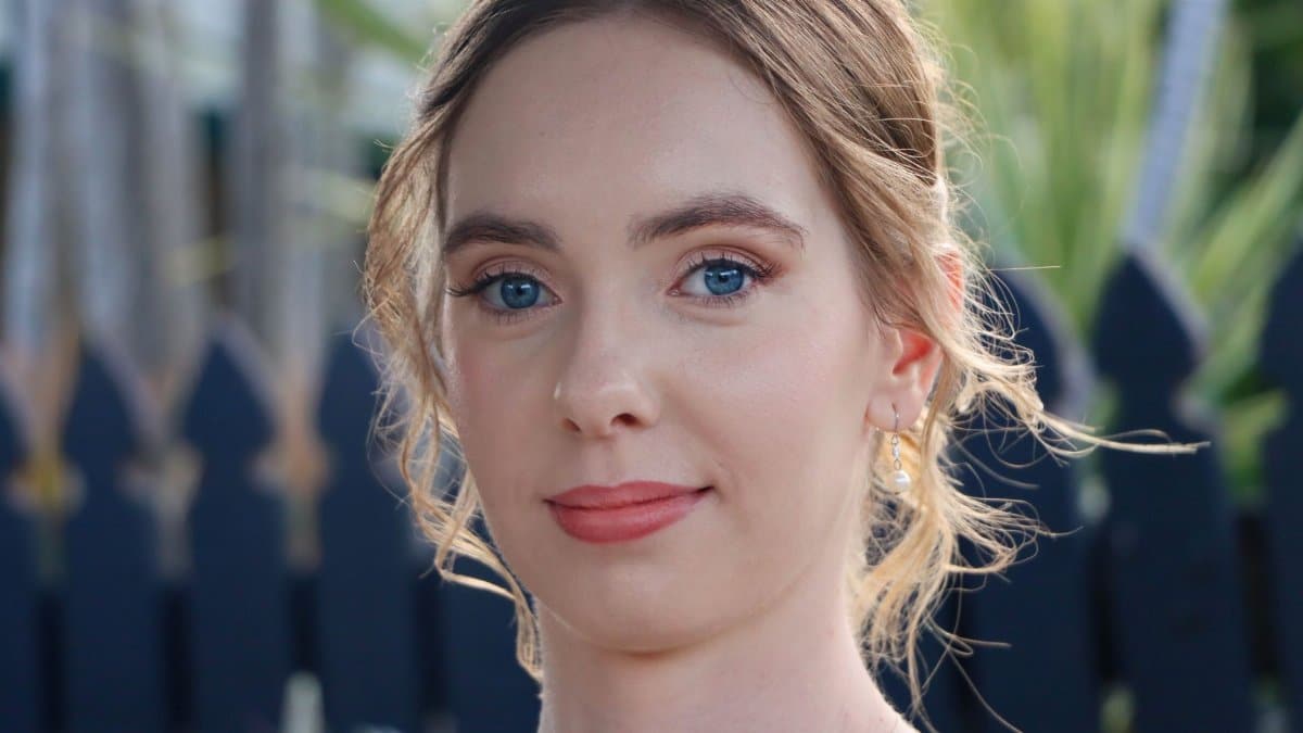 Close-up portrait of a young woman with blue eyes and natural makeup, shot outdoors.