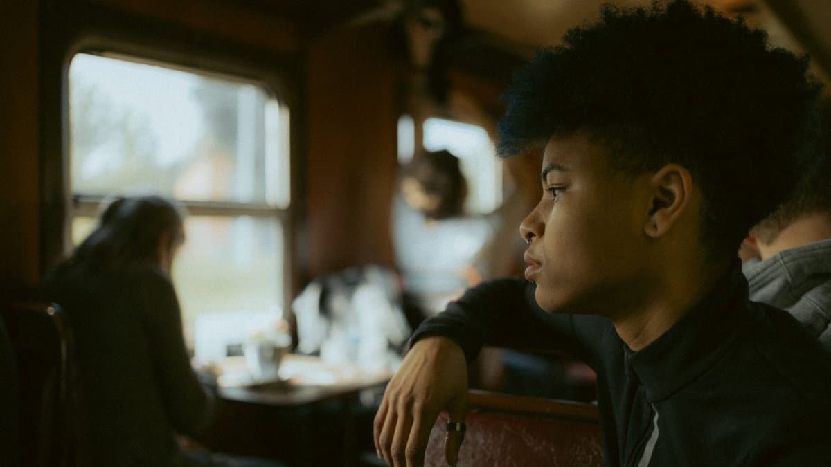 Young adult with afro hair gazing out train window, deep in thought during travel.