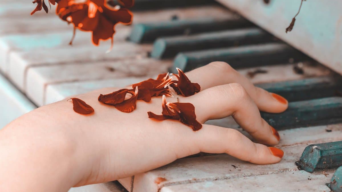 Aesthetic close-up of a hand resting on piano keys adorned with vibrant petals.