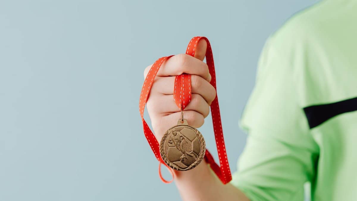 Close-up of a teenager holding a soccer medal on a red ribbon against a blue background.