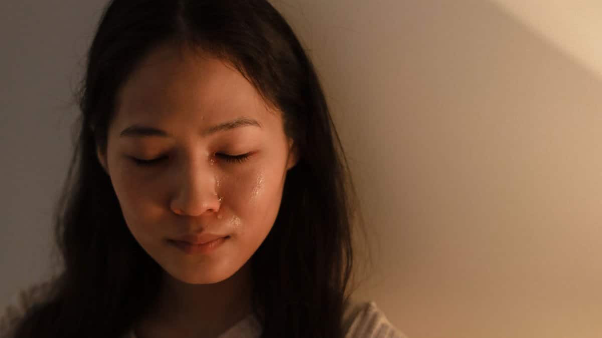 A woman with closed eyes and tears on her face, highlighting emotions of sadness indoors.