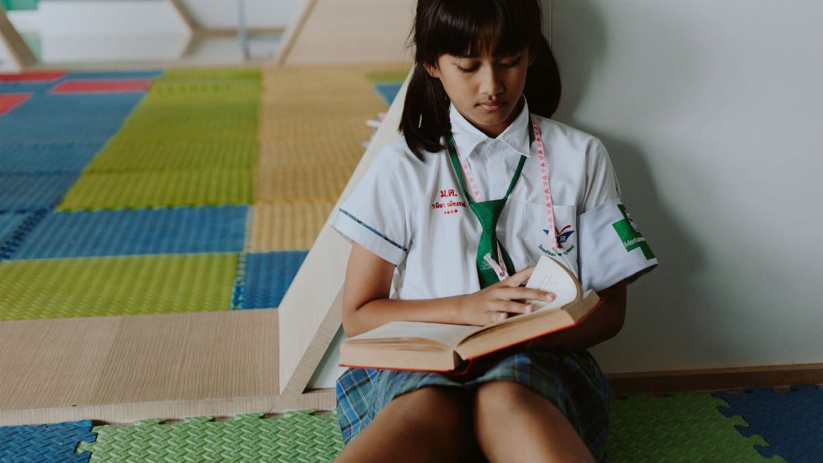A student in a school uniform reading while sitting on the colorful classroom floor.