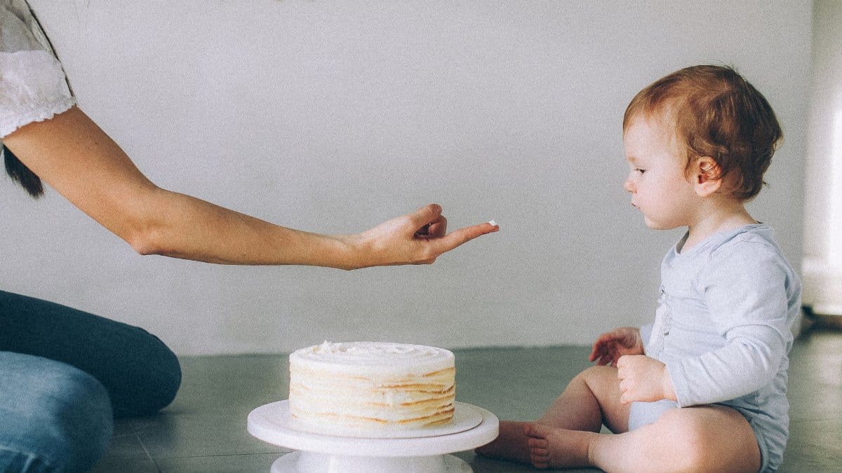 A baby experiencing his first birthday cake with a loving family member indoors.