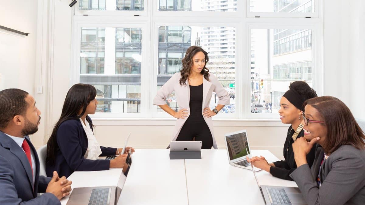 A diverse group of professionals engaged in a meeting at a modern office with laptops and city view.
