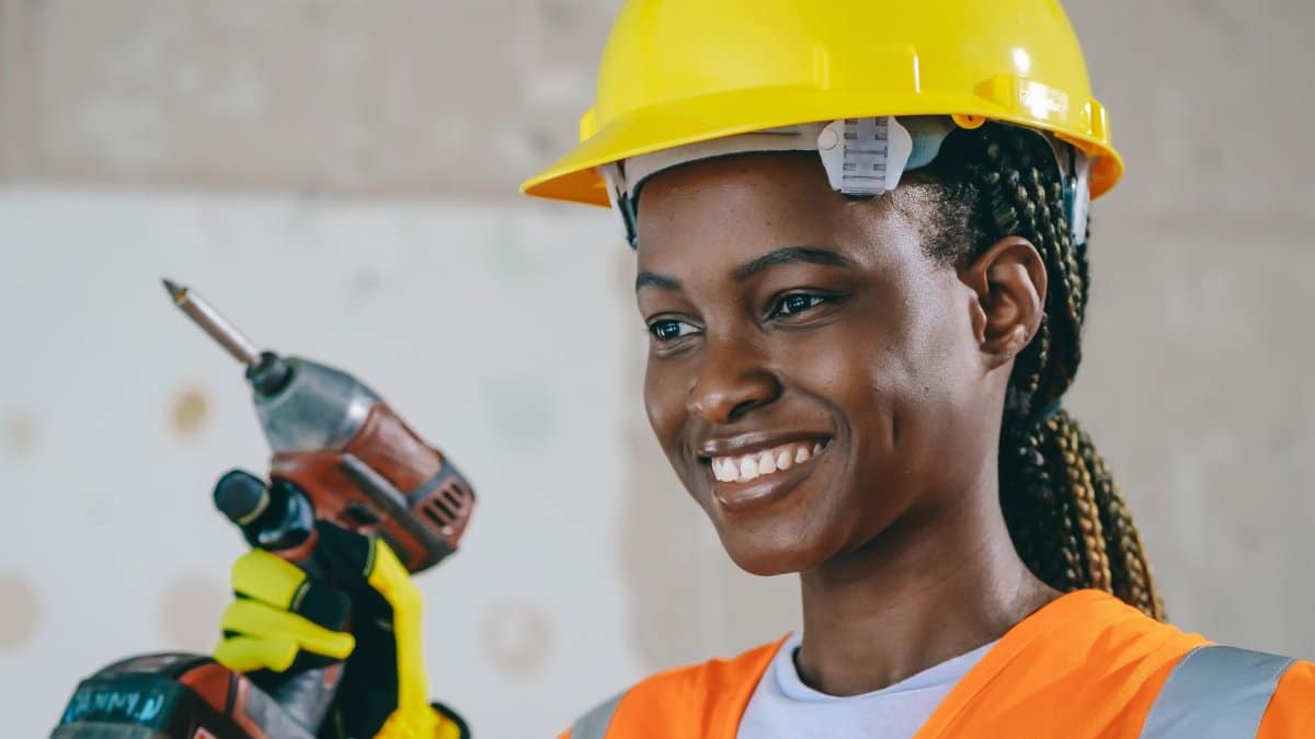 Confident female construction worker in safety gear smiling indoors.