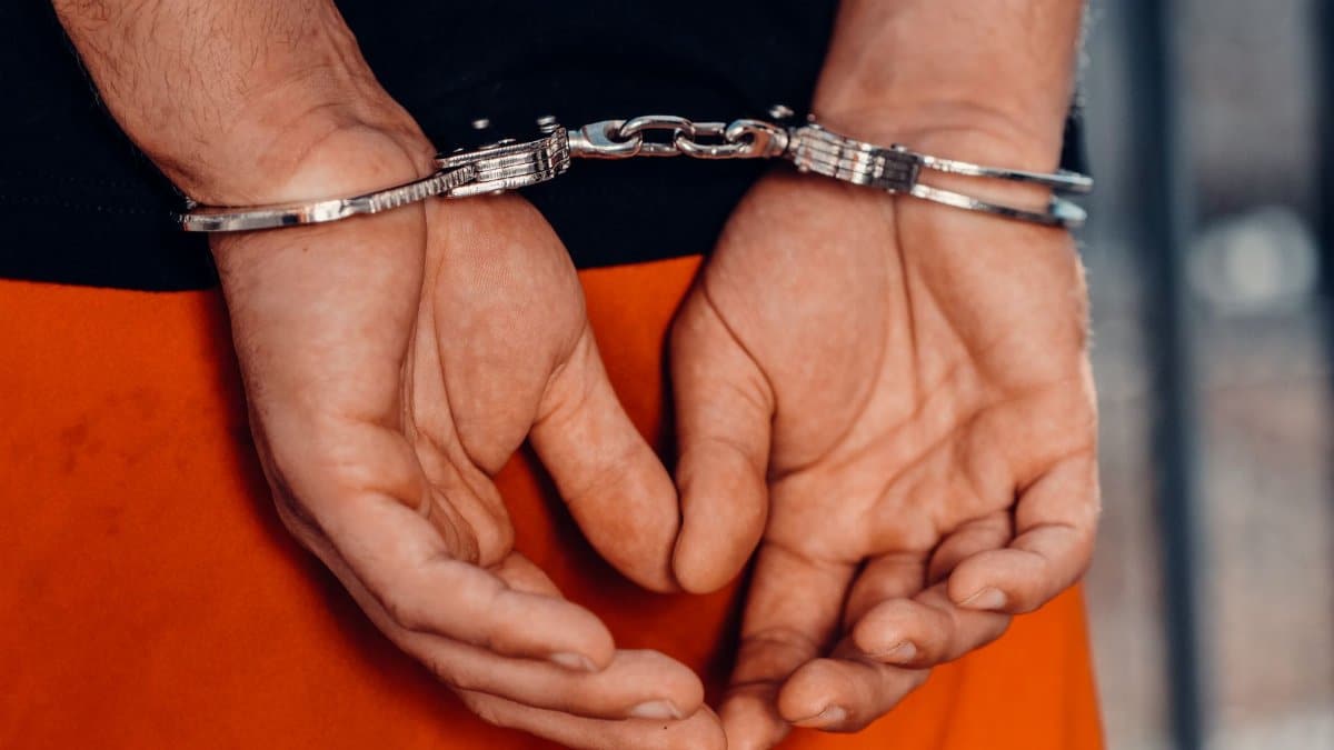 Rear view of handcuffed person in orange uniform, highlighting law enforcement and justice themes.