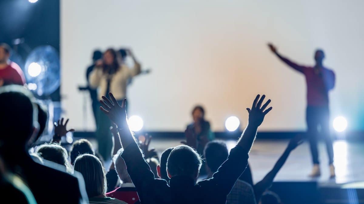 Crowd with raised hands enjoying a live indoor concert with performers on stage.