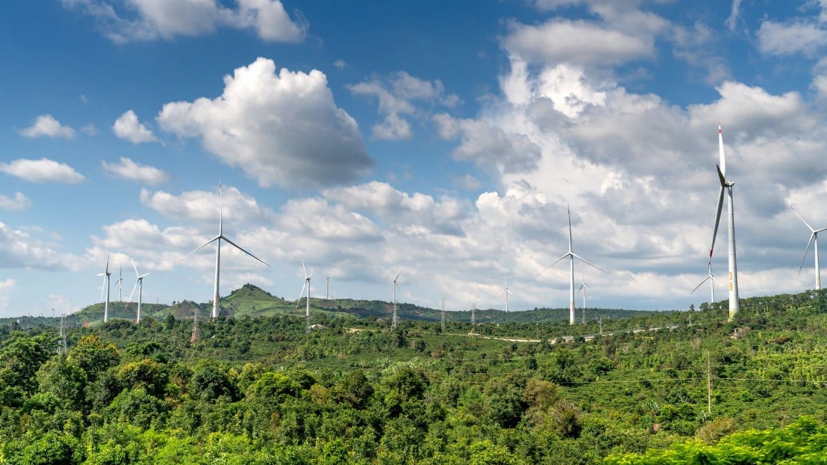 Scenic view of wind turbines on lush green hills, symbolizing renewable energy under a partly cloudy blue sky.