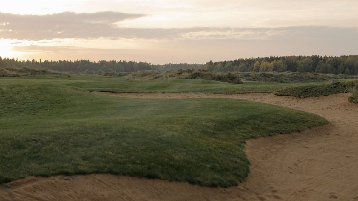 A tranquil golf course landscape at sunset, showcasing green fairways and gentle sandtraps.