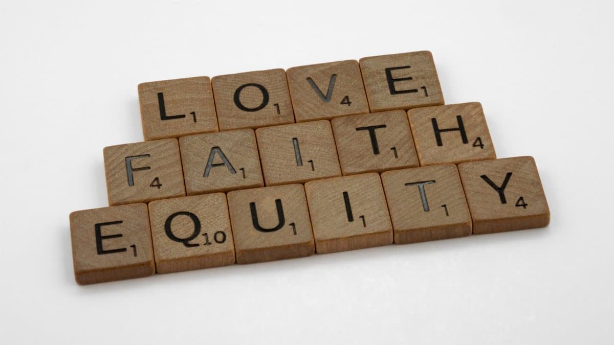 Close-up of wooden Scrabble tiles spelling Love, Faith, and Equity on a white surface.