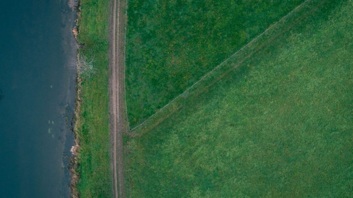 Aerial view of lush green fields and a winding path along a water body in Germany.