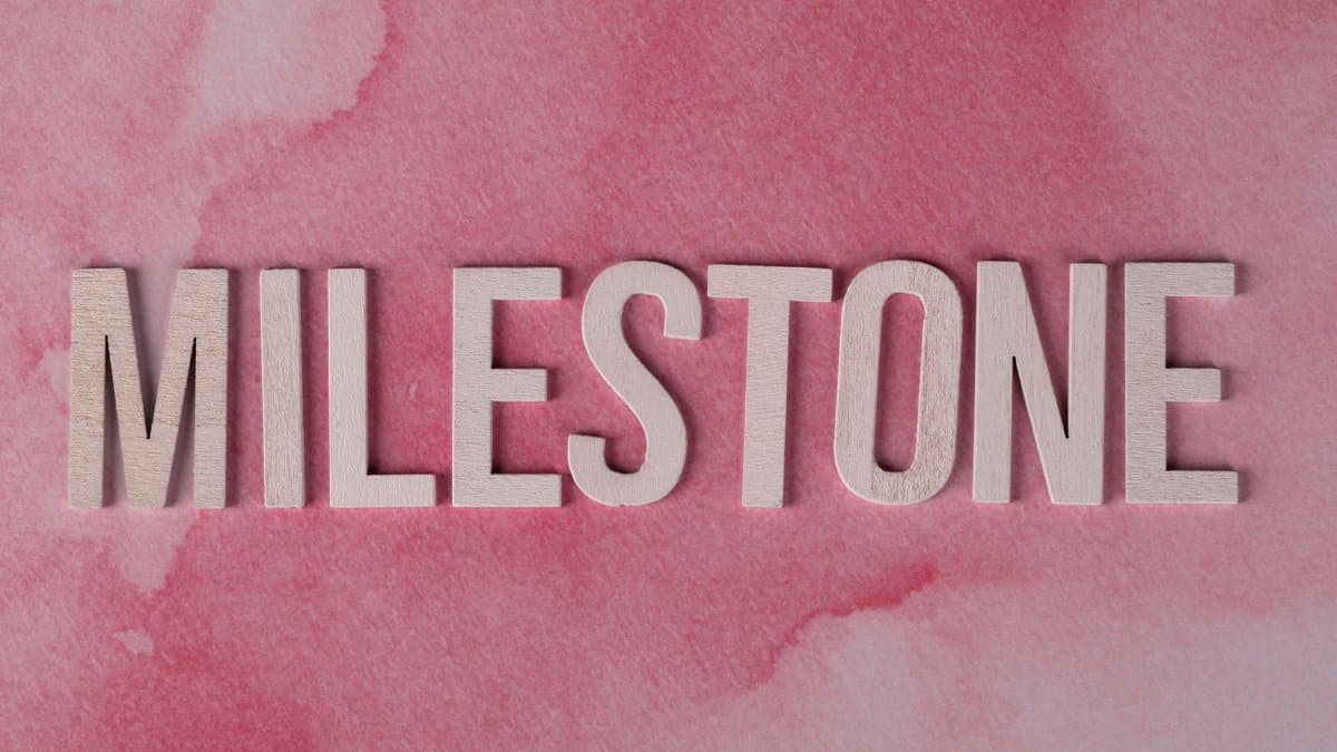 Wooden MILESTONE text on a pink watercolor background, perfect for celebrations or achievements.