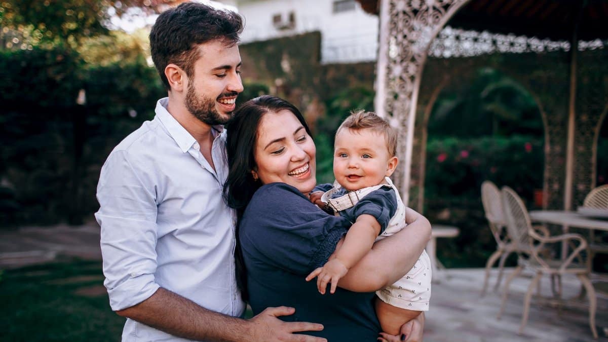 A smiling family of three enjoys an outdoor moment in a garden setting.