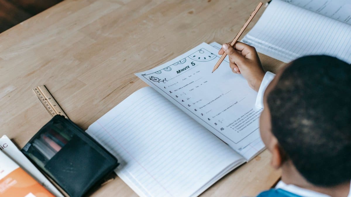 From above crop unrecognizable African American schoolboy doing test assignment while sitting at desk in light classroom