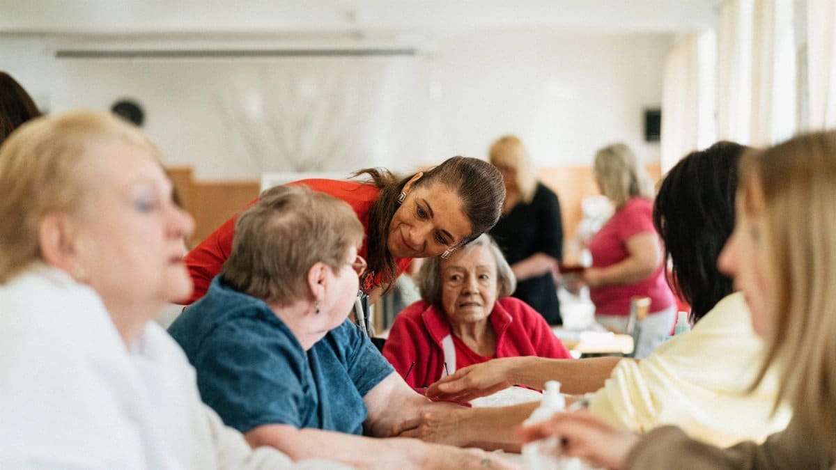 Smiling caregivers and seniors engage over a table at a community center.