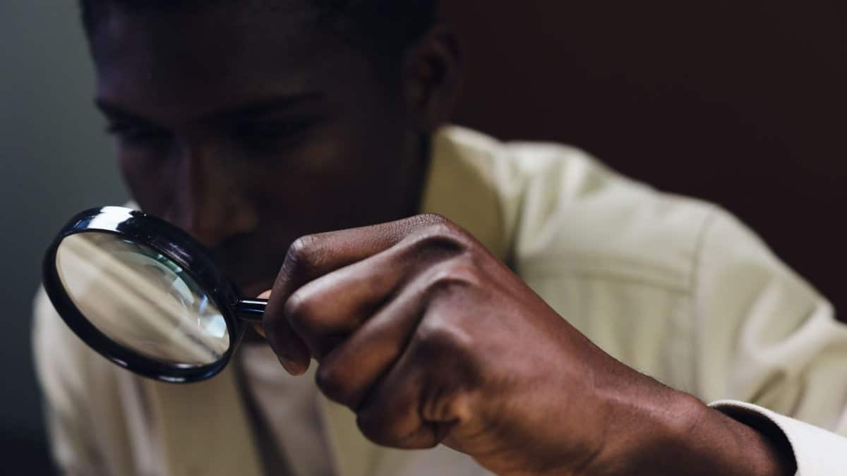 A man closely inspects an object using a magnifying glass.