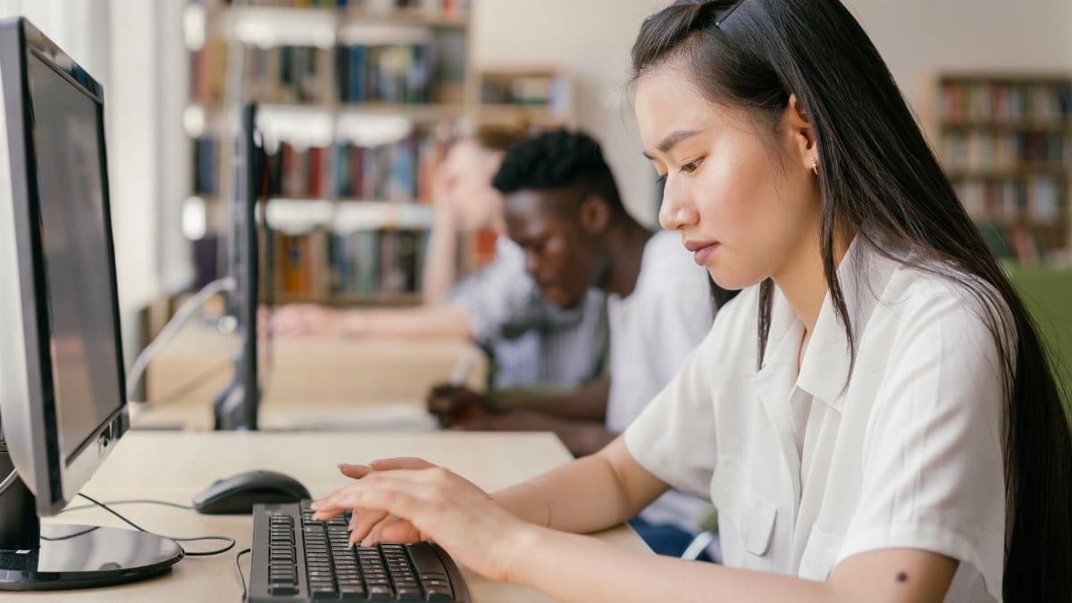 Students using computers in a library, focused on academic research and learning.