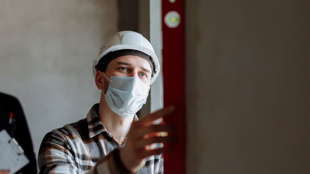 Man wearing a face mask and hard hat conducting safety inspection indoors.