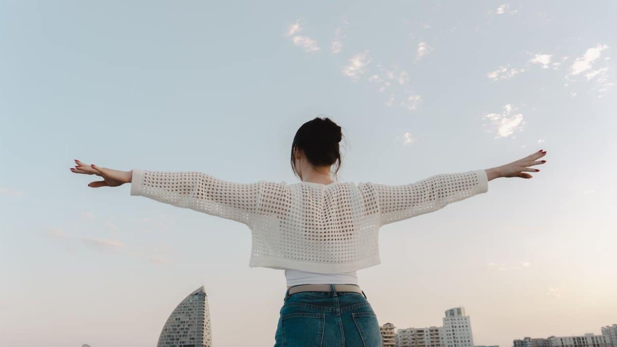 A woman with outstretched arms enjoys sunset against a modern city skyline.