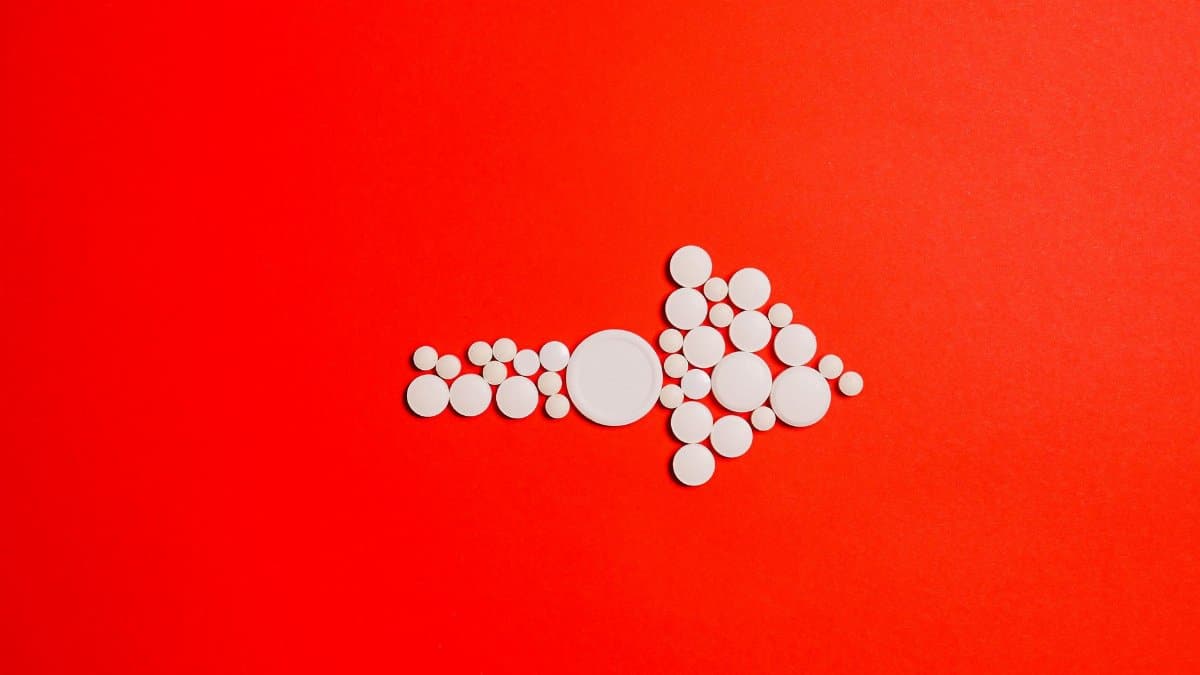 White pills form an arrow shape on a bold red backdrop, symbolizing direction in healthcare.