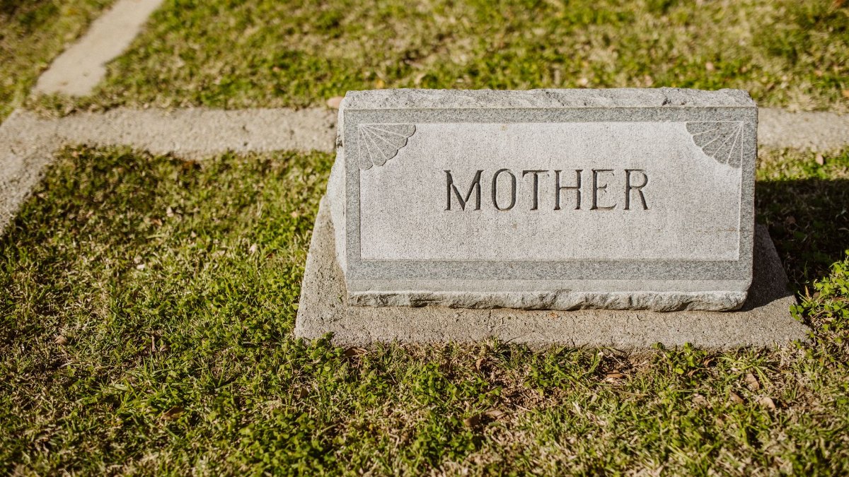 Gravestone in cemetery engraved with the word 'Mother' on grass.