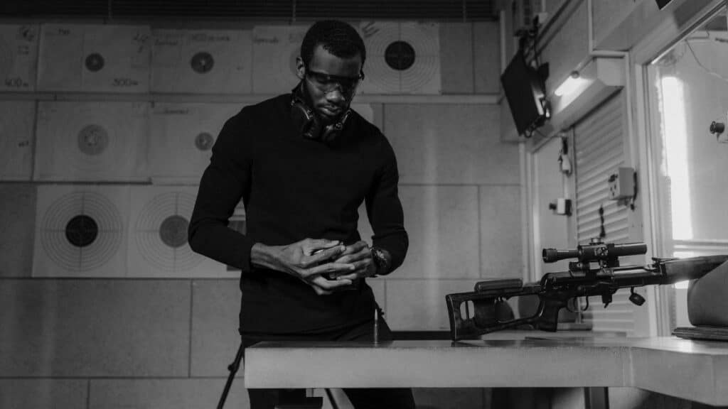 Black and white photo of a man handling a firearm at an indoor shooting range.