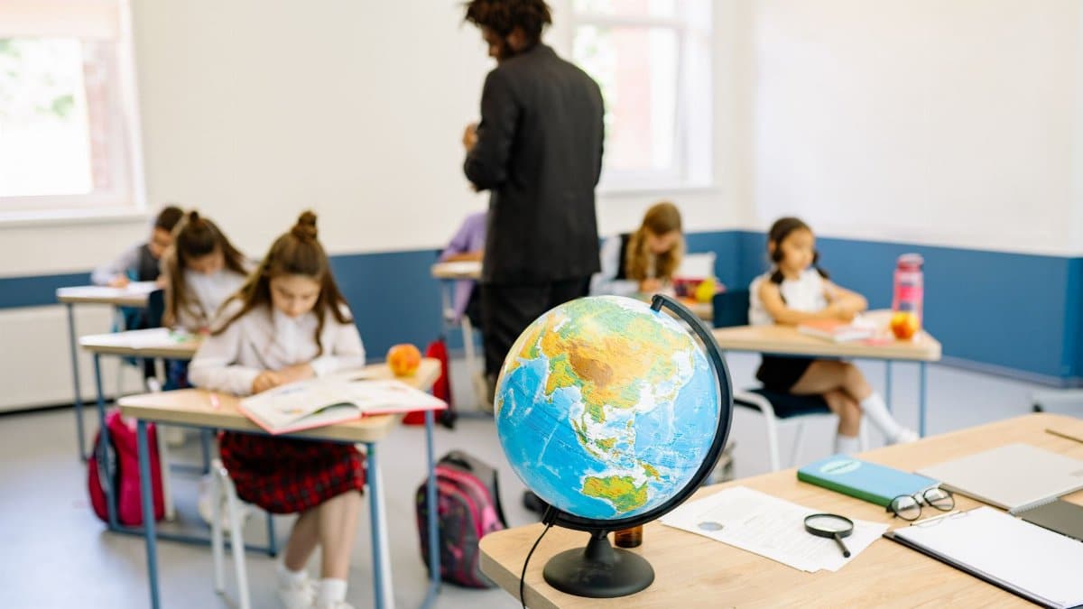 A classroom scene with students studying geography, highlighted by a prominent globe on the teacher's desk.