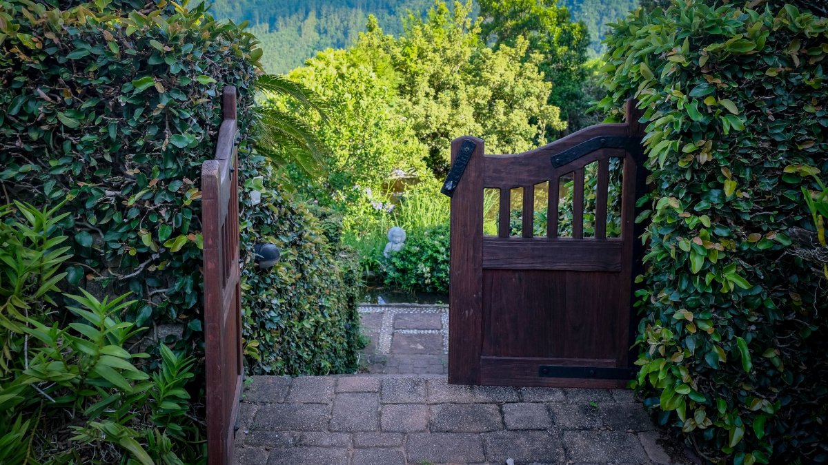 Open wooden gate leading to a lush garden with scenic mountain views.