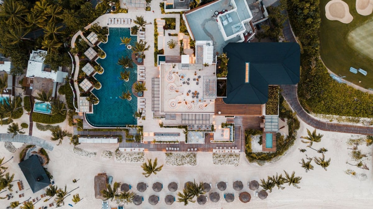 Aerial shot of a luxurious beachfront resort in Playa del Carmen, showcasing pools, loungers, and the sandy beach.