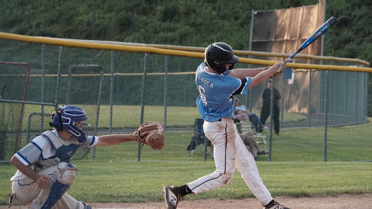 Youth baseball player swings the bat during a game on a sunny day.