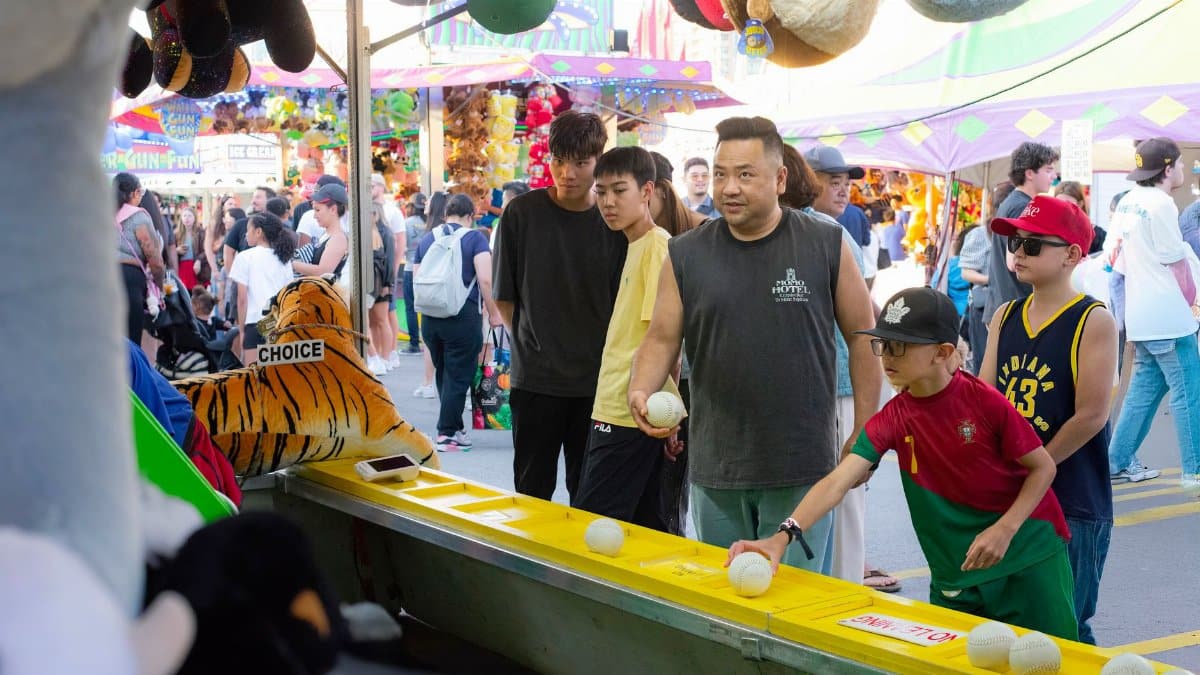 A diverse group of people engages in a fun carnival game, surrounded by vibrant festival activities.