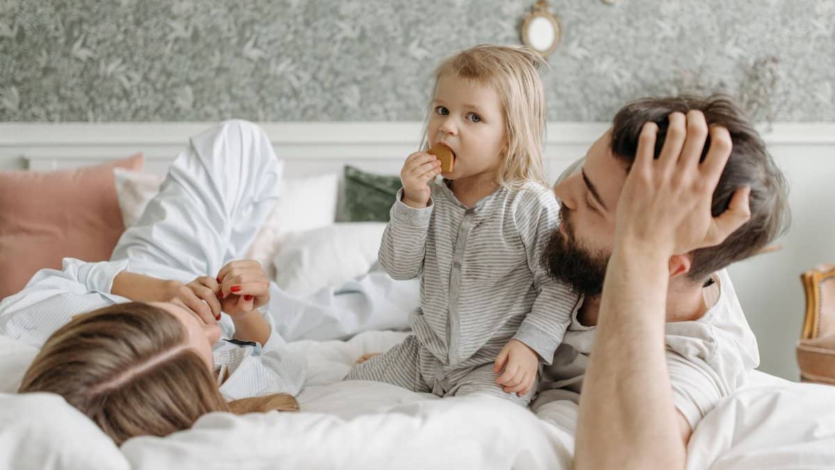 A cheerful family morning with parents and child relaxing in bed, enjoying a snack.