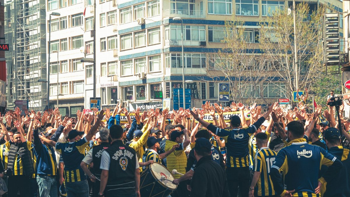 Soccer fans in blue and yellow jerseys cheer passionately in a city street with raised hands.