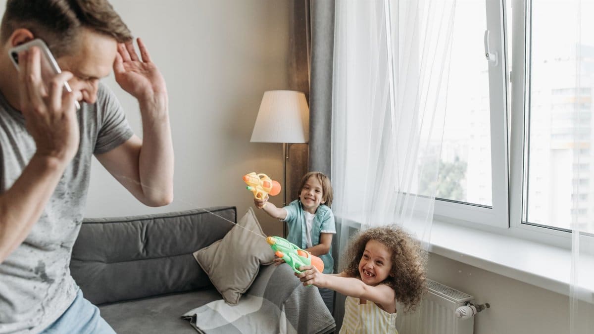 Father and children enjoying playful bonding time indoors, using water guns for fun and laughter.