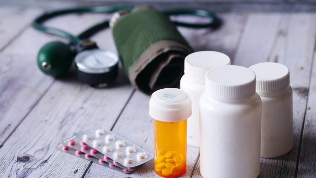 Close-up of medical supplies including pill bottles and a blood pressure monitor on a wooden surface.