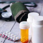 Close-up of medical supplies including pill bottles and a blood pressure monitor on a wooden surface.