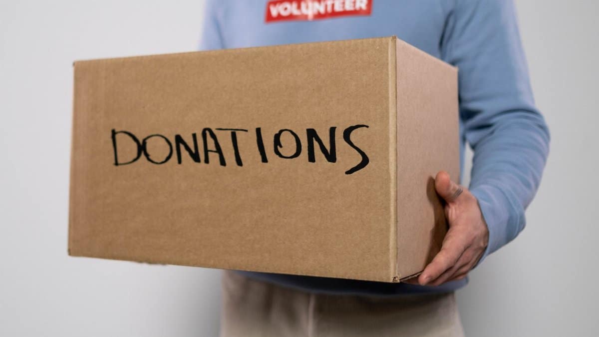 Close-up of a volunteer in a blue sweater holding a donation box. Concept of charity and volunteerism.