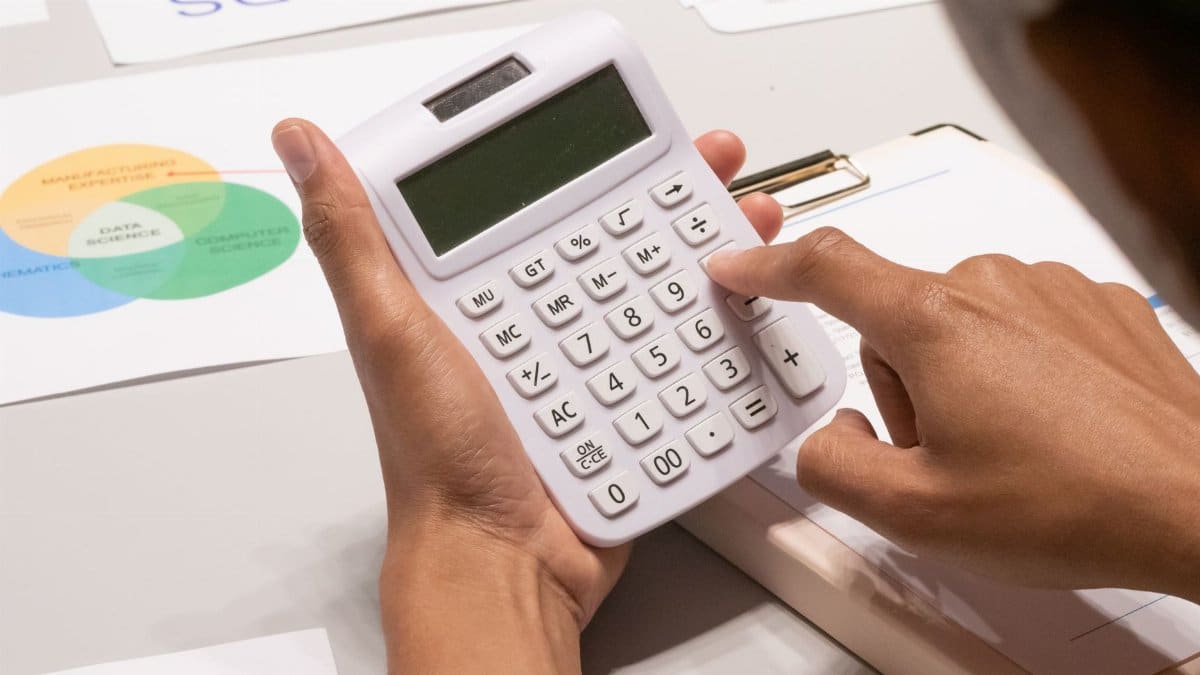 Close-up of a person's hand using a calculator on a desk with financial documents.