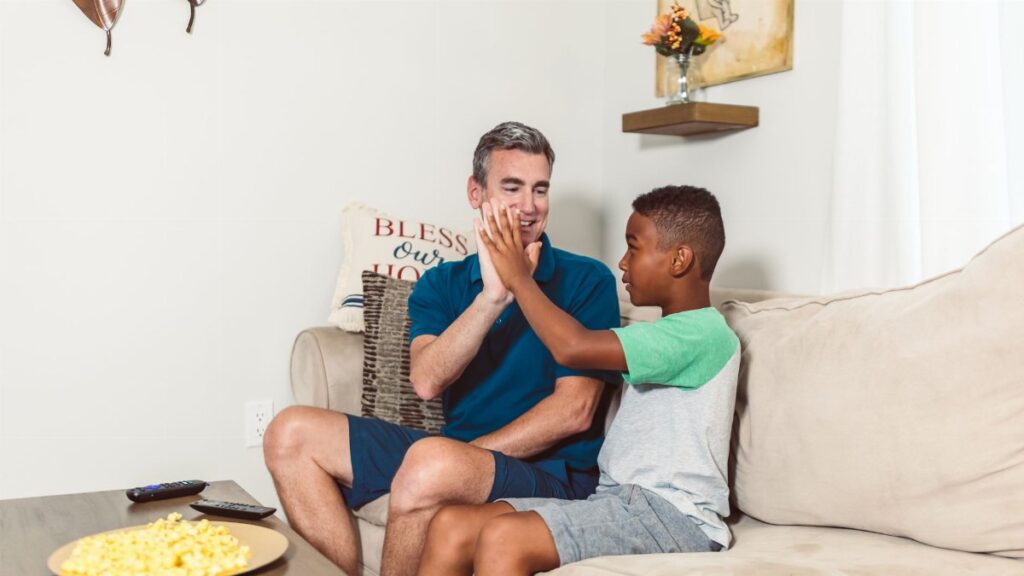 A father and son enjoying quality time on the couch, sharing a heartfelt high five.