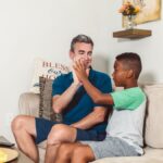 A father and son enjoying quality time on the couch, sharing a heartfelt high five.