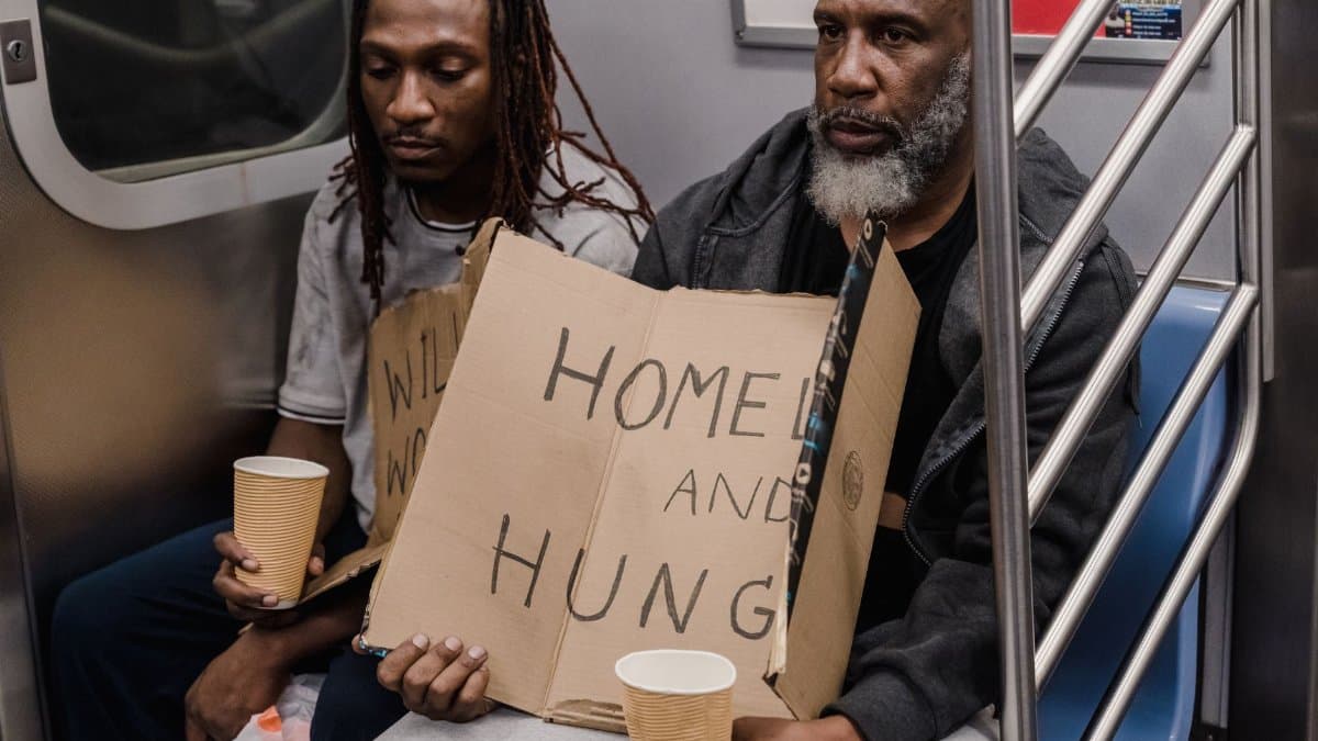Two men holding signs about homelessness in a subway train emphasize urban hardship.