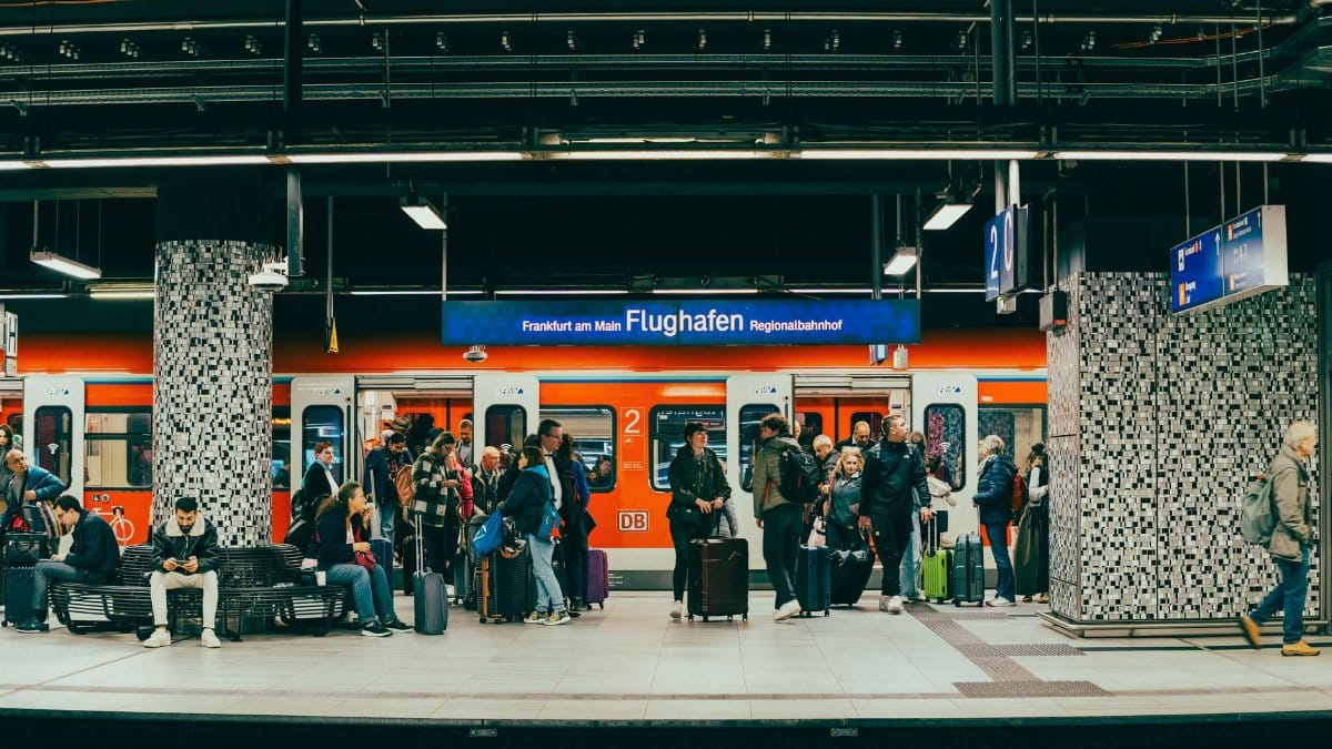 Passengers wait on the platform at Frankfurt am Main Flughafen train station with a regional train in the background.