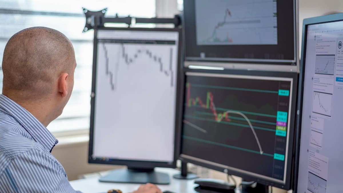 Trader analyzing financial data on multiple monitors in an office setting.