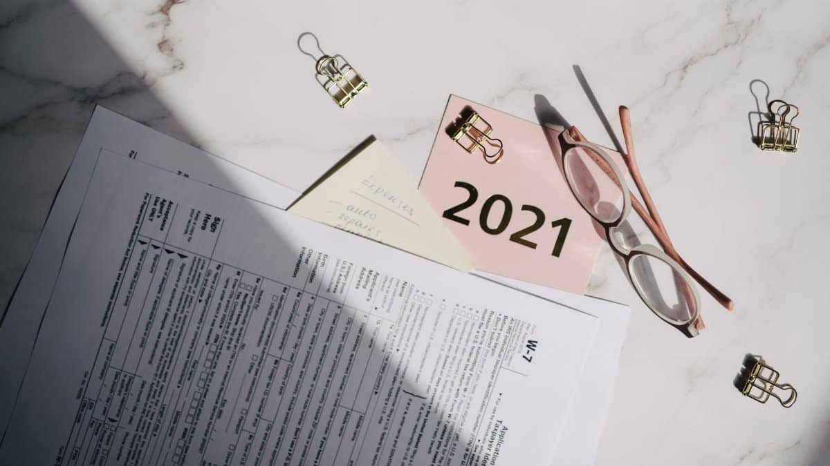 Close-up of tax documents, glasses, and a note labeled 2021 on a marble desk.