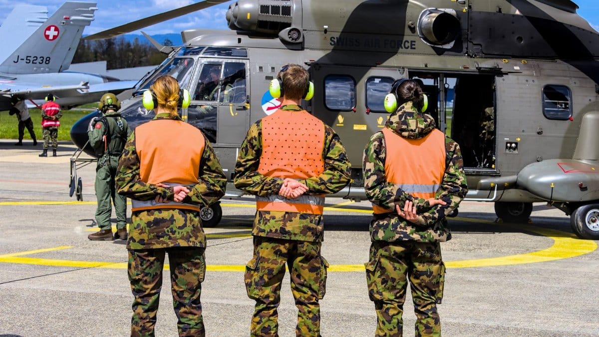 Swiss Air Force personnel in uniform at Payerne base, standing by a military helicopter.