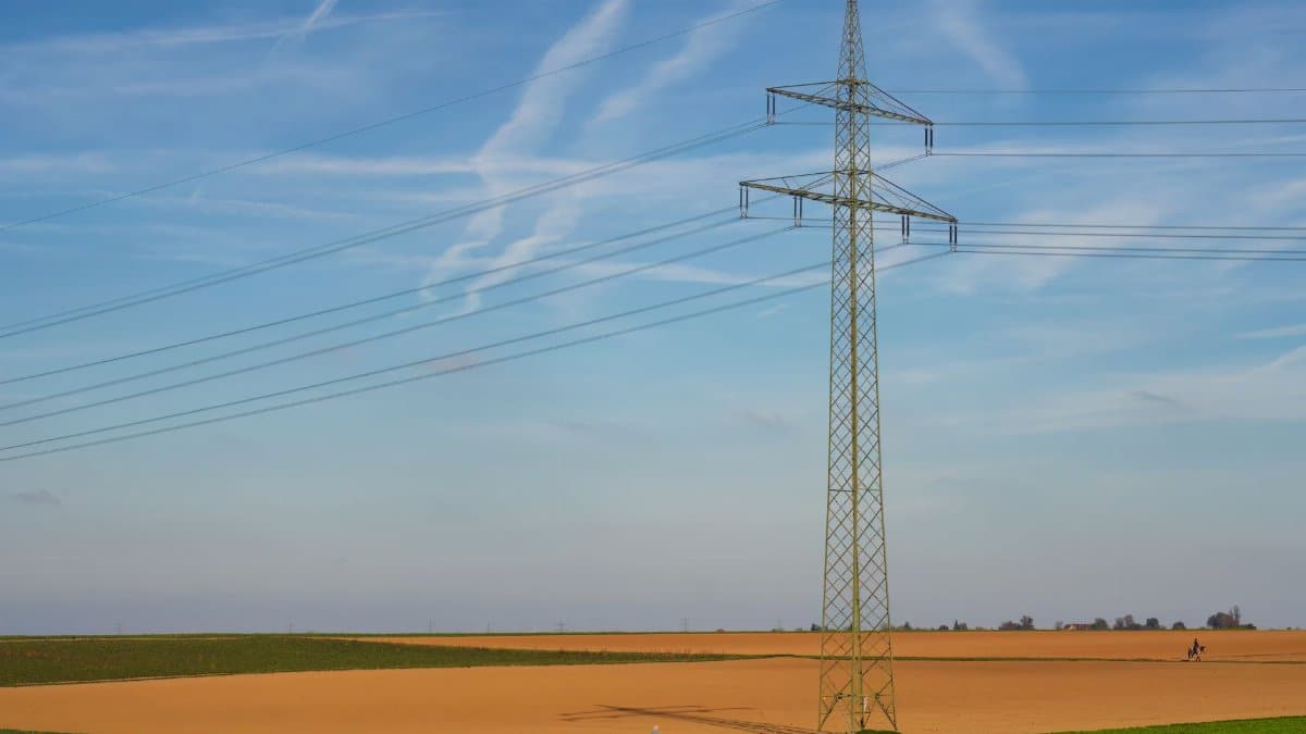 High voltage power line standing tall in a vast agricultural field under a clear blue sky in Germany.