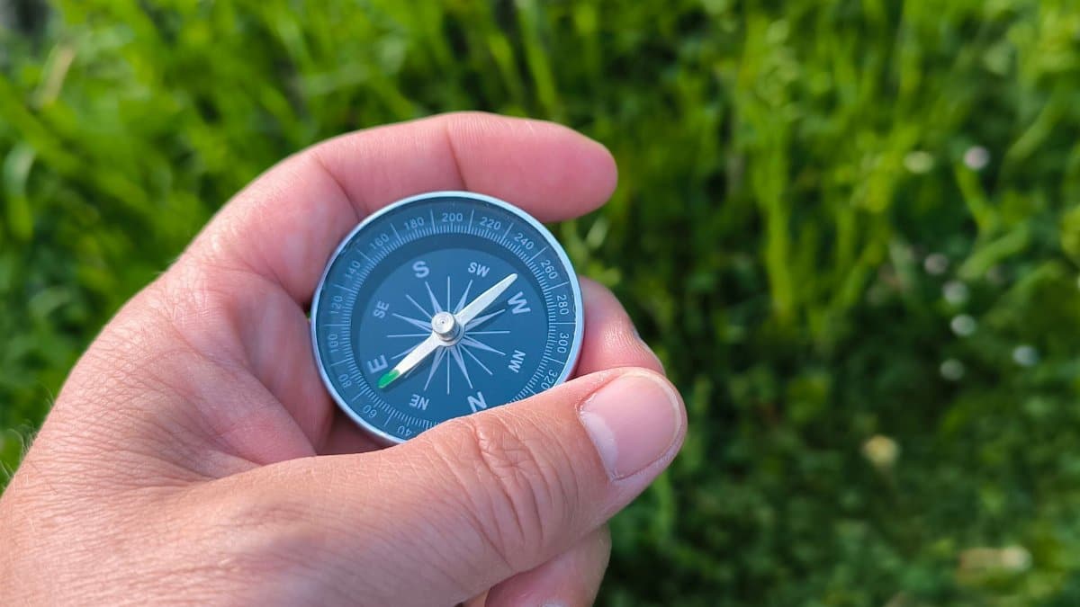 Close-up of a hand holding a compass with a green field in the background.