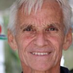 Close-up portrait of a smiling senior man with bright eyes and white hair.