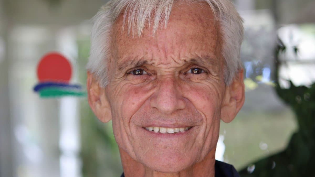 Close-up portrait of a smiling senior man with bright eyes and white hair.