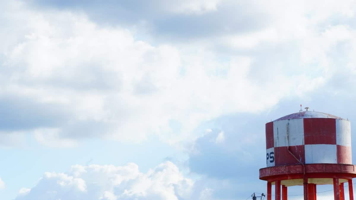 A scenic view of a red and white water tower under a blue, cloudy sky in San Marcos, Texas.
